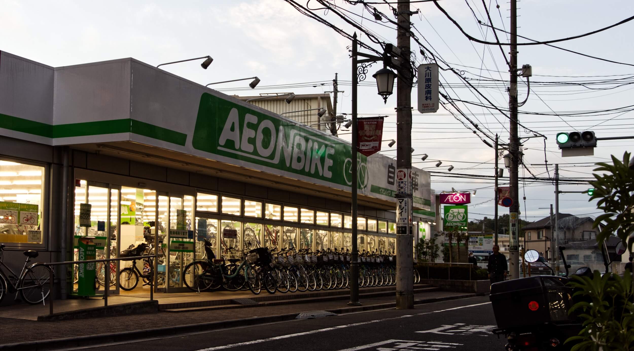 A bike shop at dusk. The interior is brightly lit and the light illuminates a row of bicycles outside