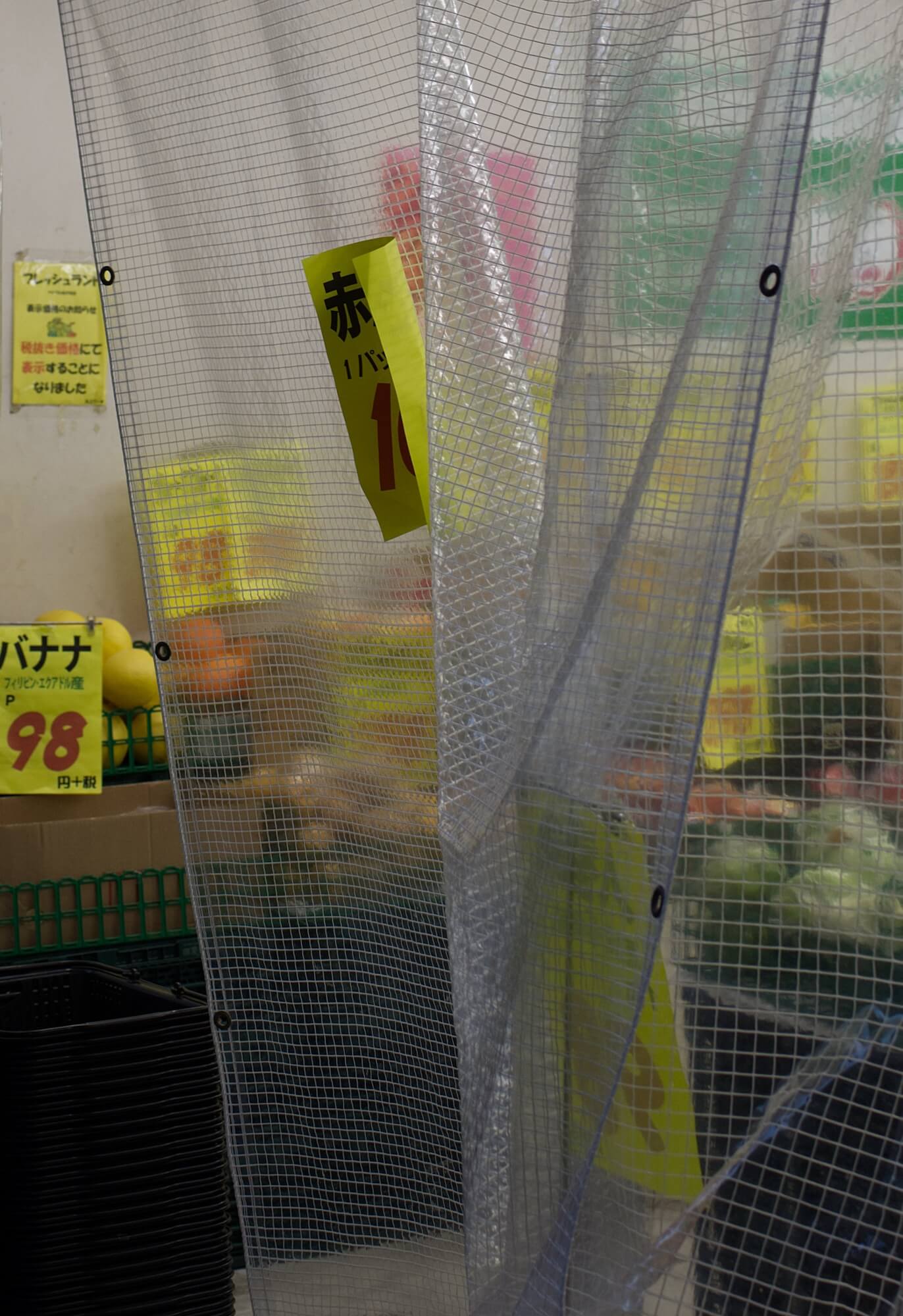 A greengrocer. A plastic sheet covers the frame and bright yellow price tags can be seen tucked amongst the produce