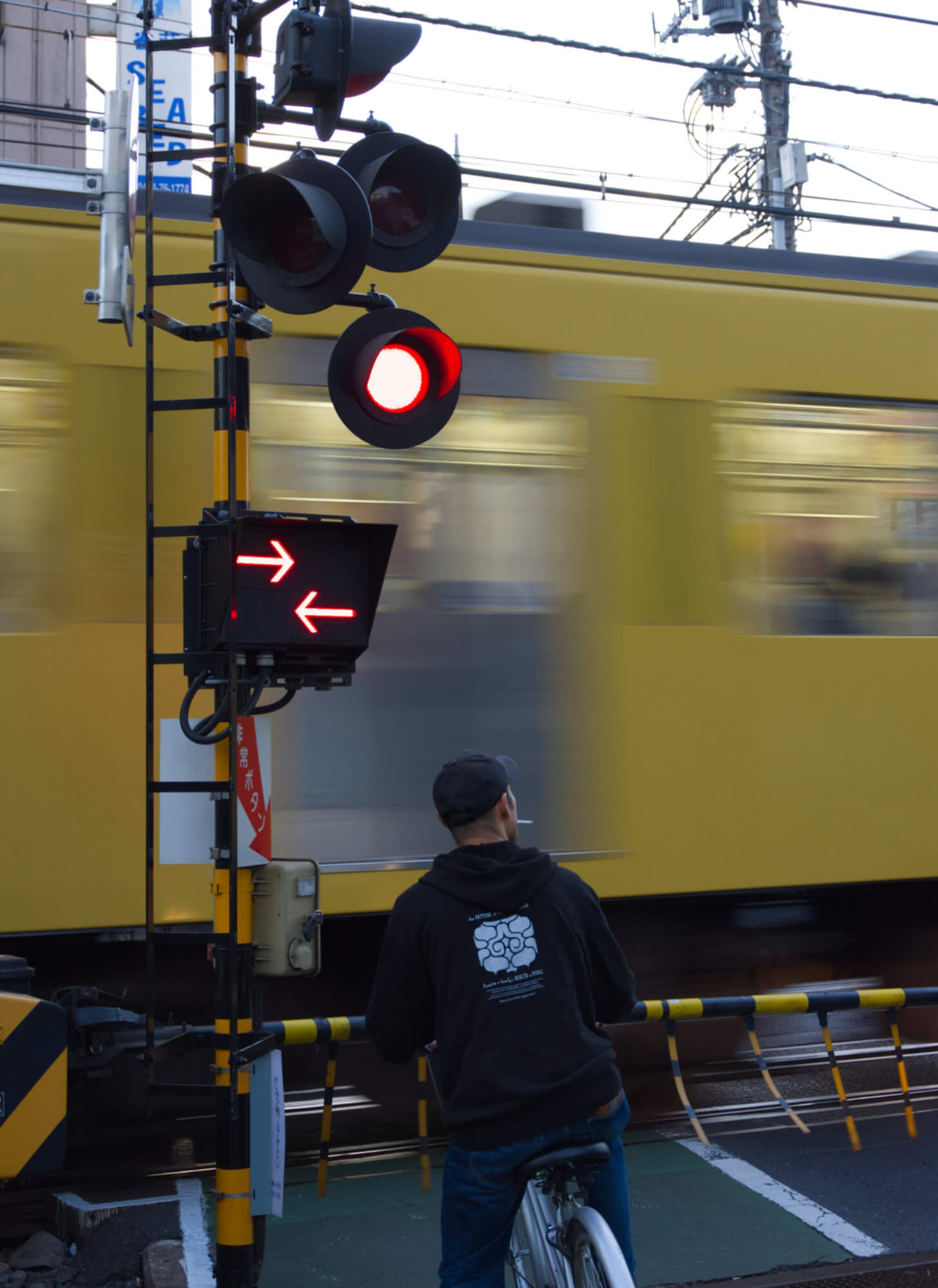 A man on a bike waits at a level crossing as a yellow train speeds past